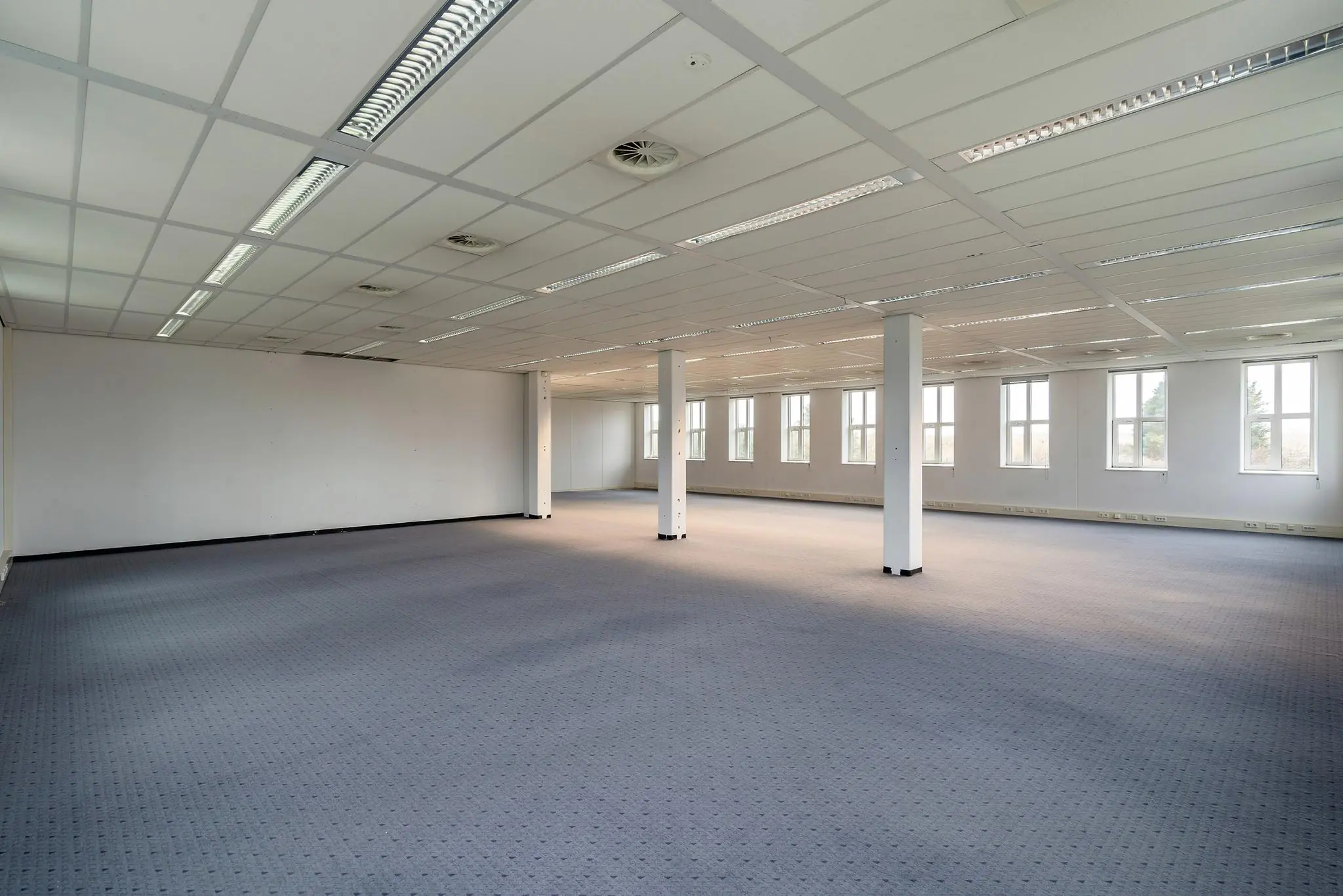 Lege kantoorruimte aan de Vareseweg met systeemplafond, tapijtvloer en grote ramen.