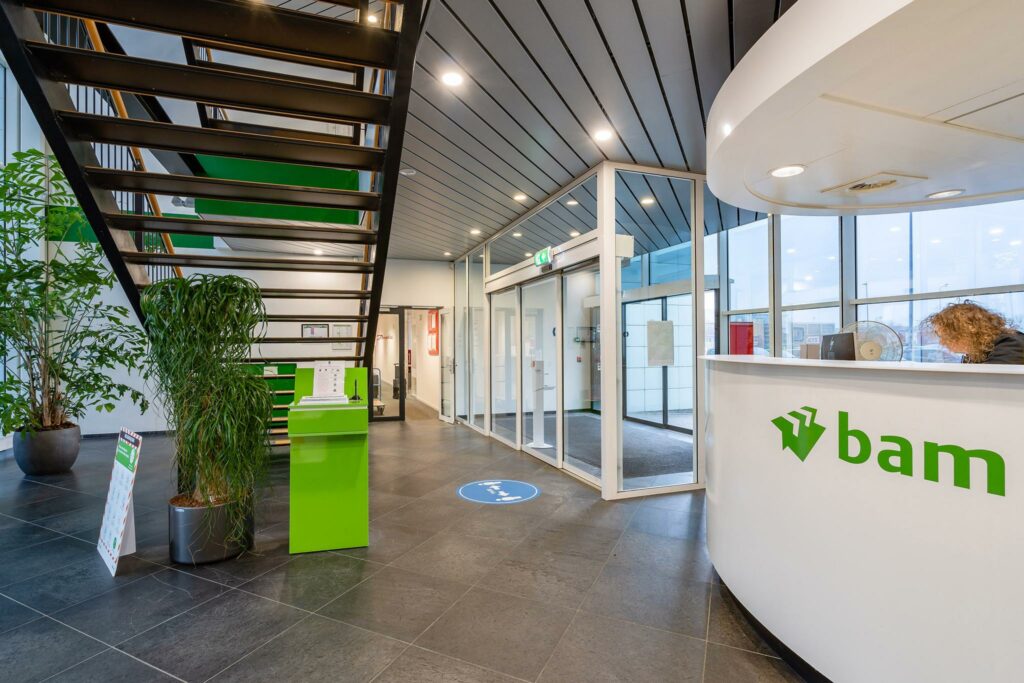 Moderne ontvangsthal van BAM aan de Vareseweg met balie, trap en glazen entree.