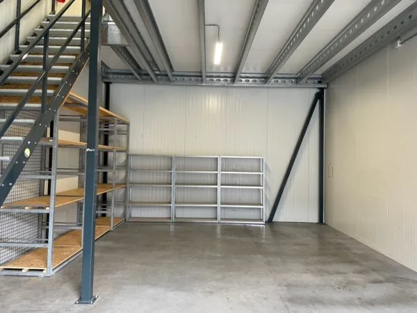 Opslagruimte aan de Aalsmeerderweg met metalen stellingen, betonnen vloer en stalen trap naar een verhoogd platform.