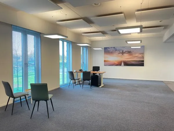 Moderne kantoorruimte met een bureau, vergaderstoelen en een grote wandfoto van een opstijgend vliegtuig boven een landingsbaan bij zonsondergang.