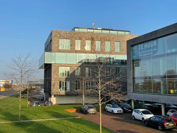 Kantoorgebouw aan de Linatebaan met glazen gevels en 'Te Huur'-bord, omgeven door geparkeerde auto's en een groen grasveld.