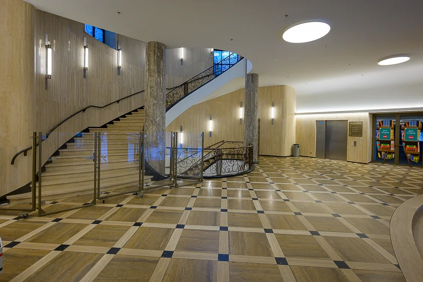 Ruime en stijlvolle hal van het stadhuis aan de Coolsingel met een marmeren trap, lift en kunstwerken naast de ingang.