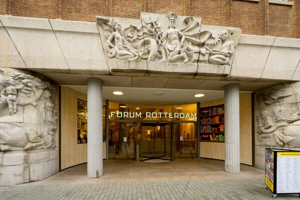 Ingang van Forum Rotterdam aan de Coolsingel, met beeldhouwwerk en een glazen draaideur.
