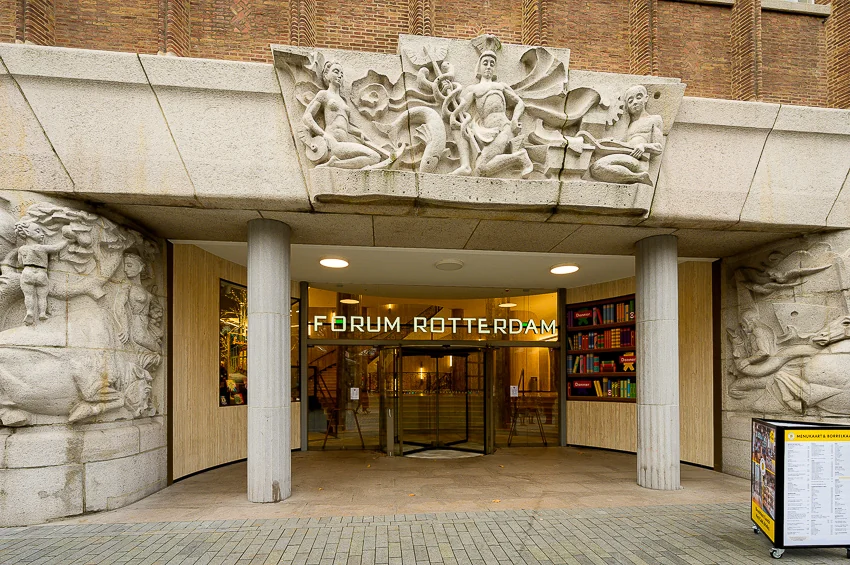 Ingang van Forum Rotterdam aan de Coolsingel, met beeldhouwwerk en een glazen draaideur.