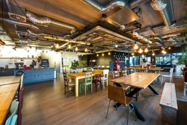 Moderne, industrieel ingerichte gezamenlijke ruimte met kitchenette en houten eettafels aan de Naritaweg.