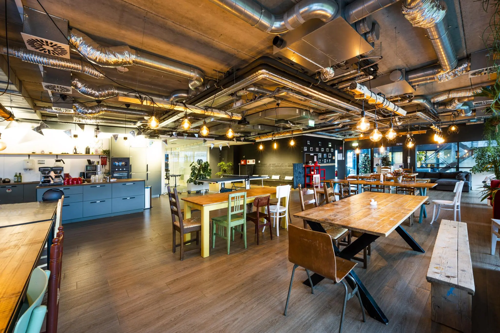 Moderne, industrieel ingerichte gezamenlijke ruimte met kitchenette en houten eettafels aan de Naritaweg.