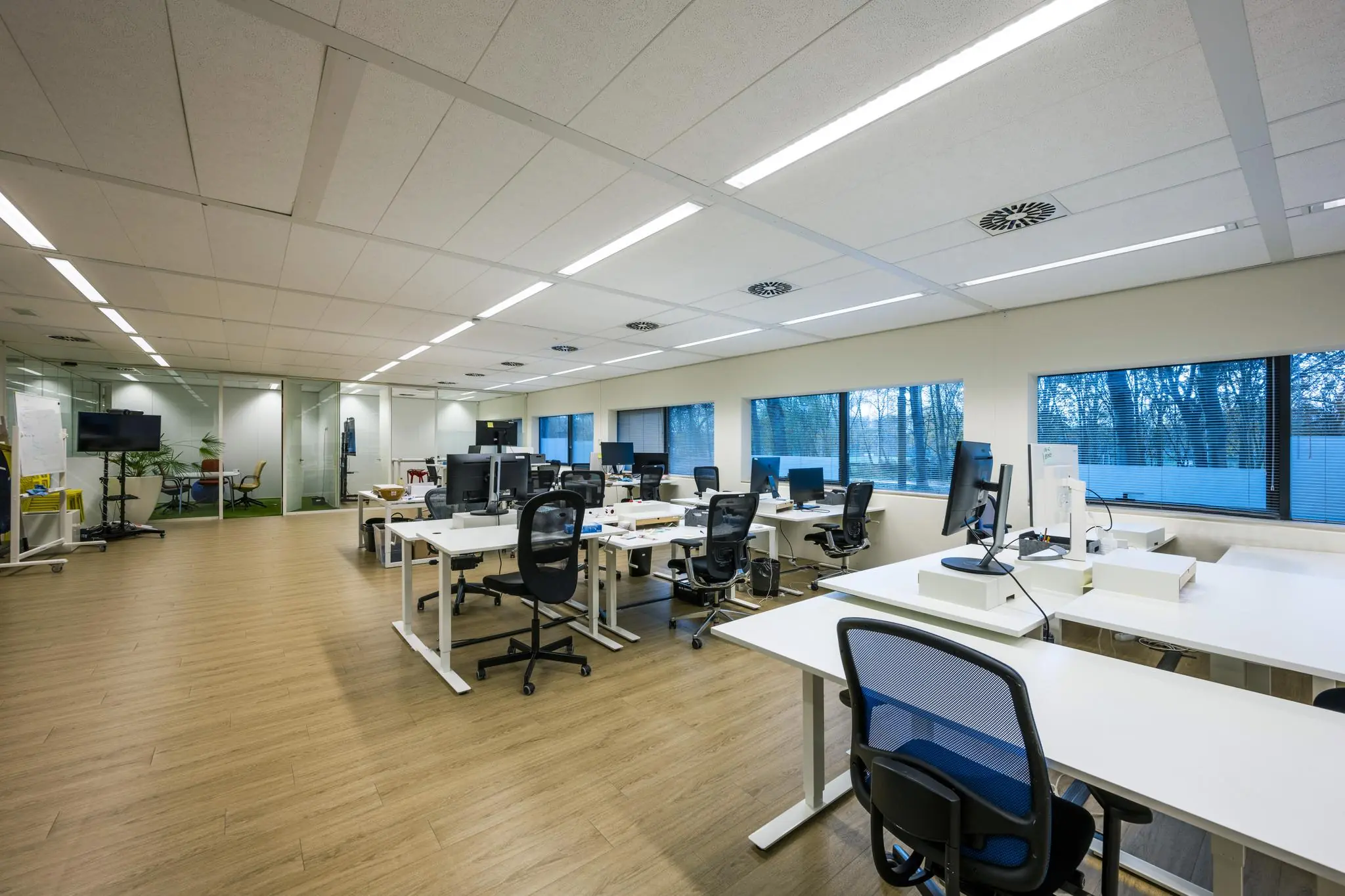 Moderne en ruime kantoortuin aan de Naritaweg met flexwerkplekken, ergonomische bureaustoelen en grote ramen met uitzicht op bomen.