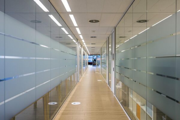 Gang in een modern kantoorgebouw aan de Naritaweg met glazen wanden en houten vloer.