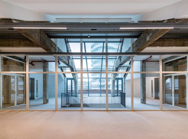 Binnenruimte met glazen wand en zicht op betonnen draagconstructie en moderne gebouwen aan de Coolsingel in Rotterdam.