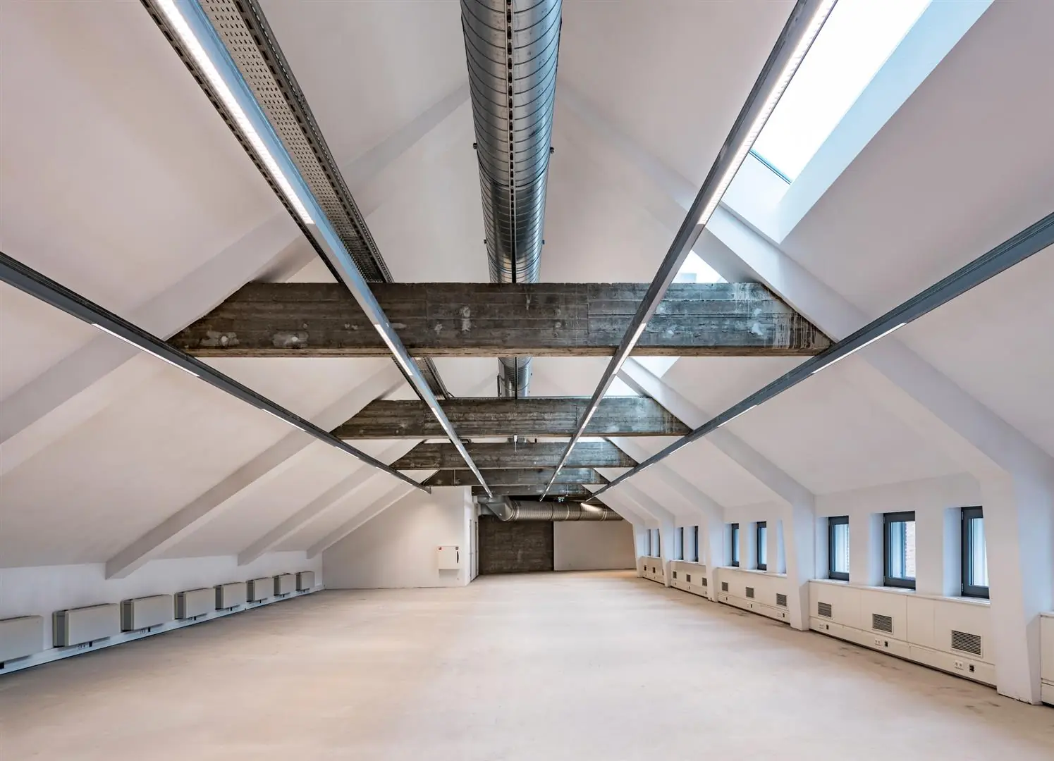 Licht en ruim zolderverdieping van een gebouw aan de Coolsingel, met betonnen balken, zichtbare ventilatiebuizen en grote dakramen.