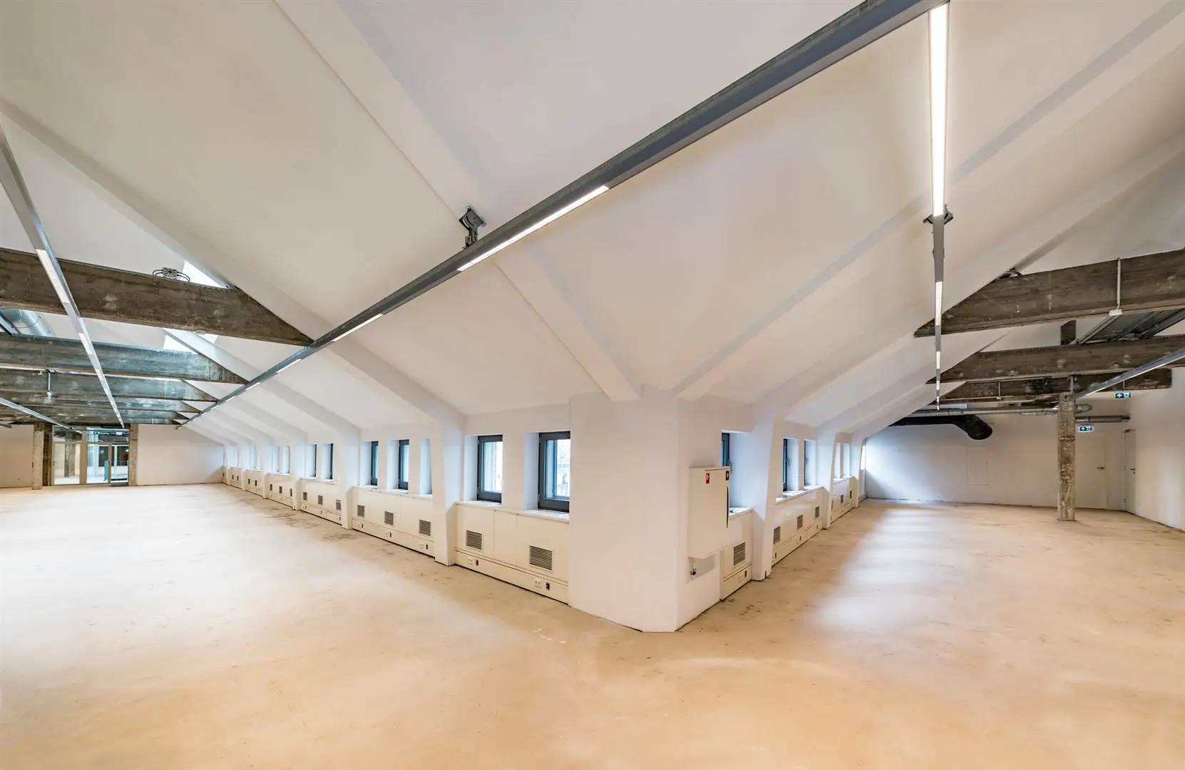 Lichte, lege kantoorruimte met schuine plafonds, betonnen balken en ramen langs beide zijden in een pand aan de Coolsingel.