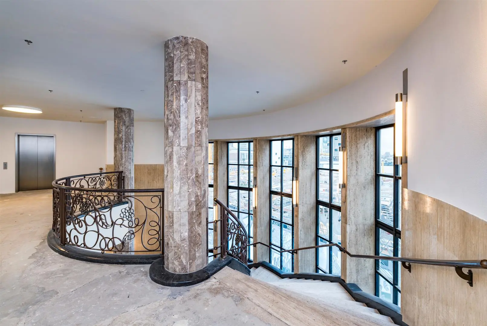 Trap met marmeren zuilen en sierlijke balustrade in het Coolsingel-gebouw, met uitzicht op grote ramen en de stad.