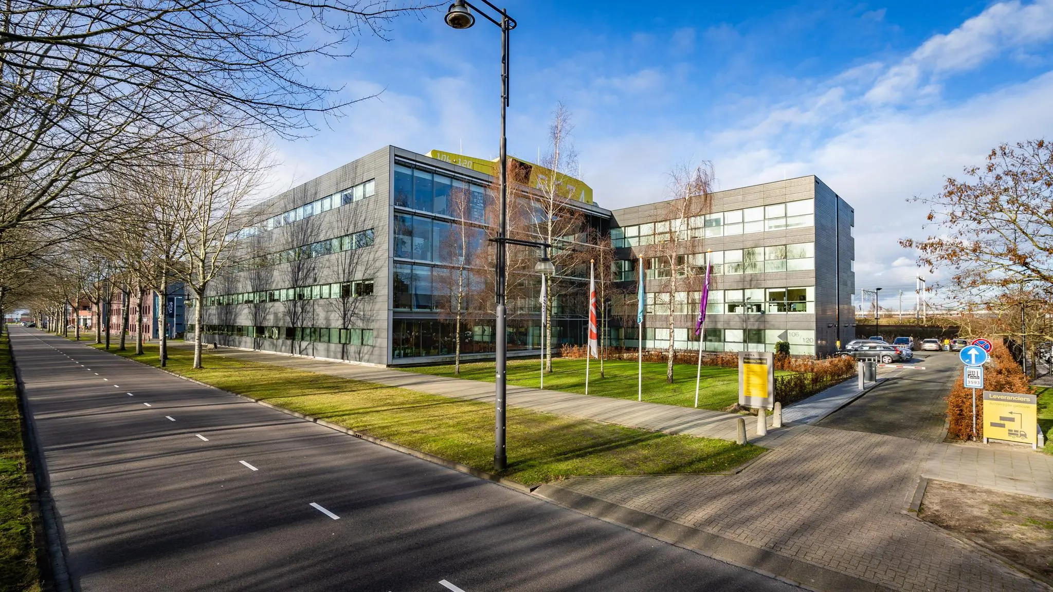 Modern kantoorgebouw aan de Naritaweg in Amsterdam met vlaggenmast en een brede toegangsweg.