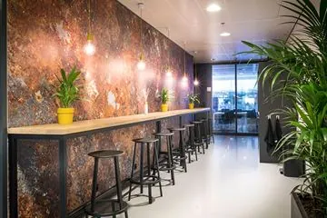 Moderne zitruimte aan het Wilhelminaplein met een lange hoge tafel, barkrukken, hanglampen en groene planten.