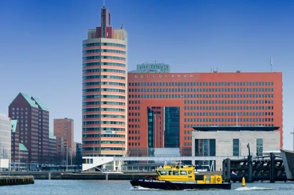 Gezicht op het Wilhelminaplein in Rotterdam met moderne hoogbouw en een gele Port of Rotterdam-boot op de voorgrond.