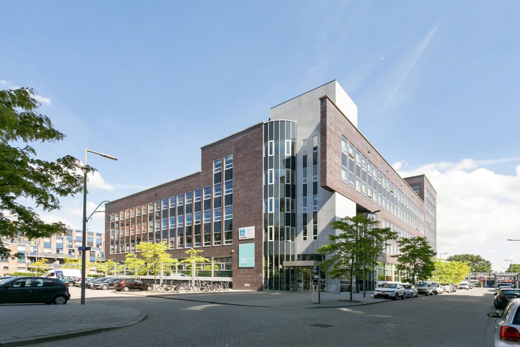 Modern kantoorgebouw aan de Dynamostraat in een stedelijke omgeving met geparkeerde auto's en fietsen.