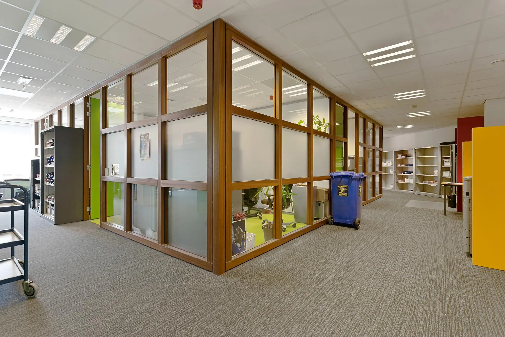 Moderne kantoorruimte aan de Dynamostraat met glazen binnenwanden, kasten en een blauwe afvalcontainer.