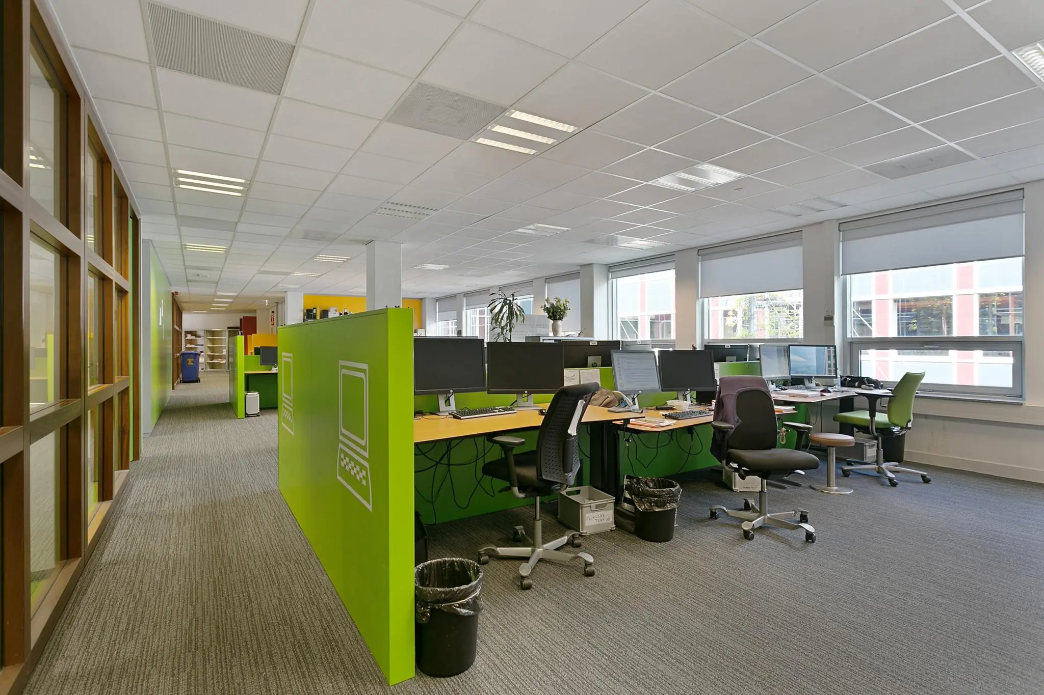 Modern kantoorinterieur aan de Dynamostraat met werkplekken, groene scheidingspanelen en grote ramen.