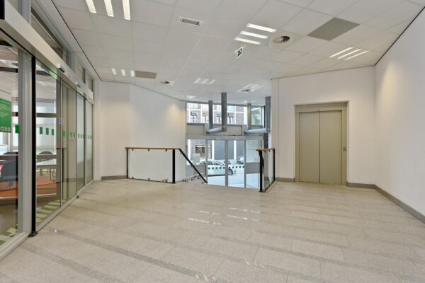 Moderne entreehal met een lift, glazen schuifdeuren en een trap naar de begane grond aan de Dynamostraat.