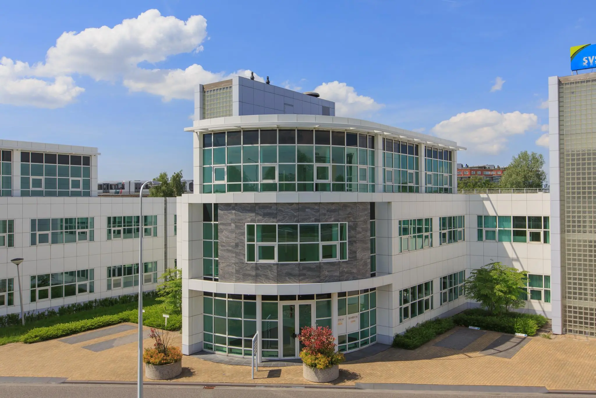 Modern kantoorgebouw aan het Rhijnspoor met witte gevel en grote raampartijen onder een blauwe lucht.