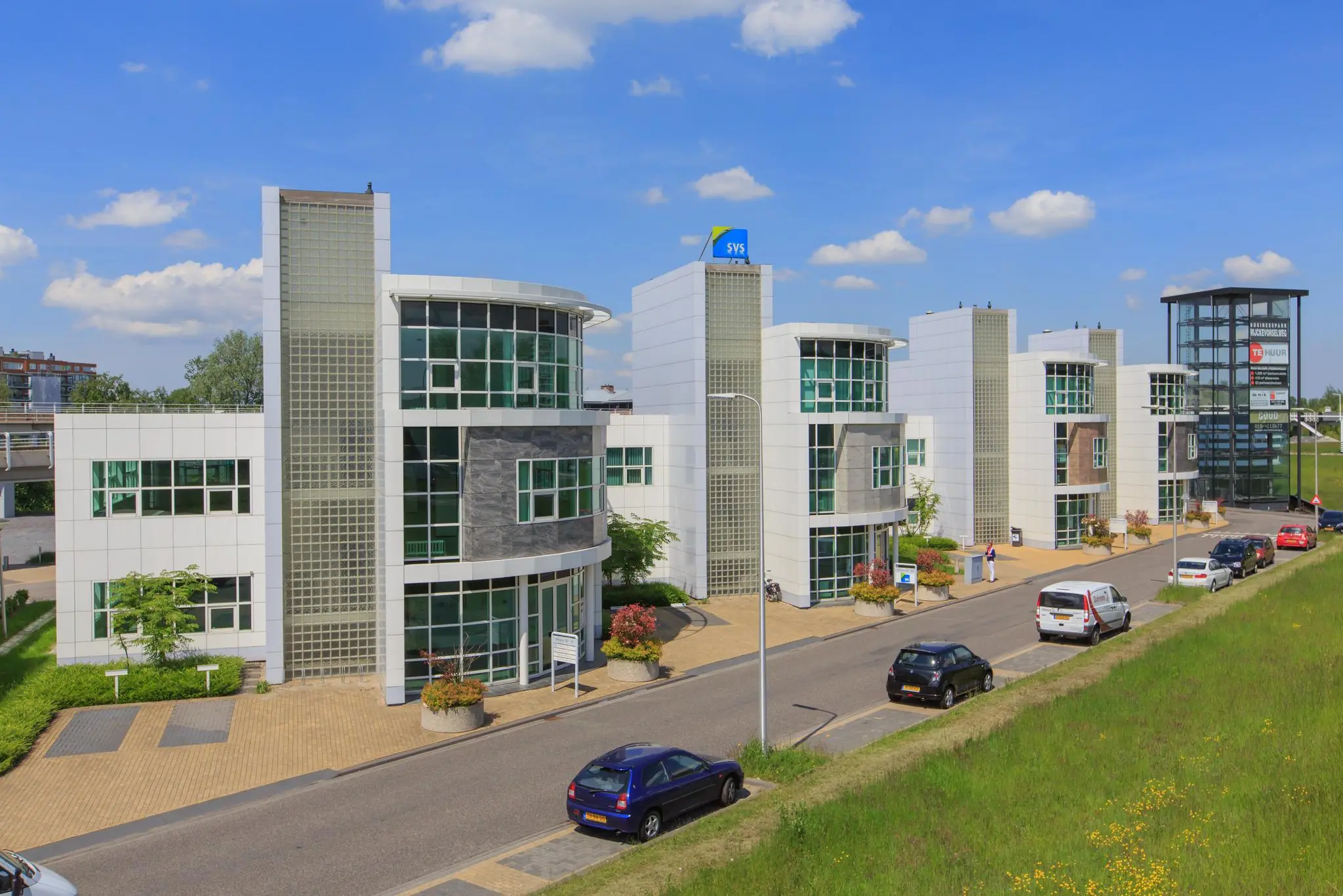 Moderne kantoorgebouwen aan het Rhijnspoor met glazen gevels en een helderblauwe lucht op de achtergrond.