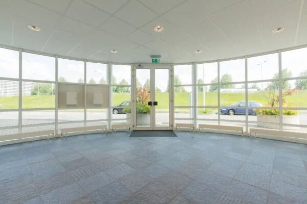 Ingang met glazen deuren en ramen van een kantoorpand aan het Rhijnspoor, met uitzicht op geparkeerde auto's en groenstrook.