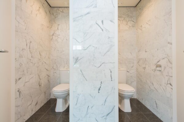 Twee moderne toiletruimtes met marmeren wanden, gescheiden door een tussenmuur.