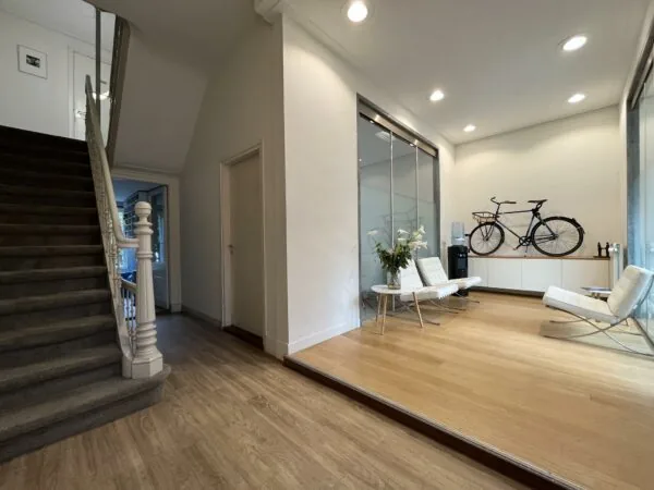 Moderne wachtruimte aan de Ramstraat met witte stoelen, een zwarte fiets aan de muur en een trap naar boven.