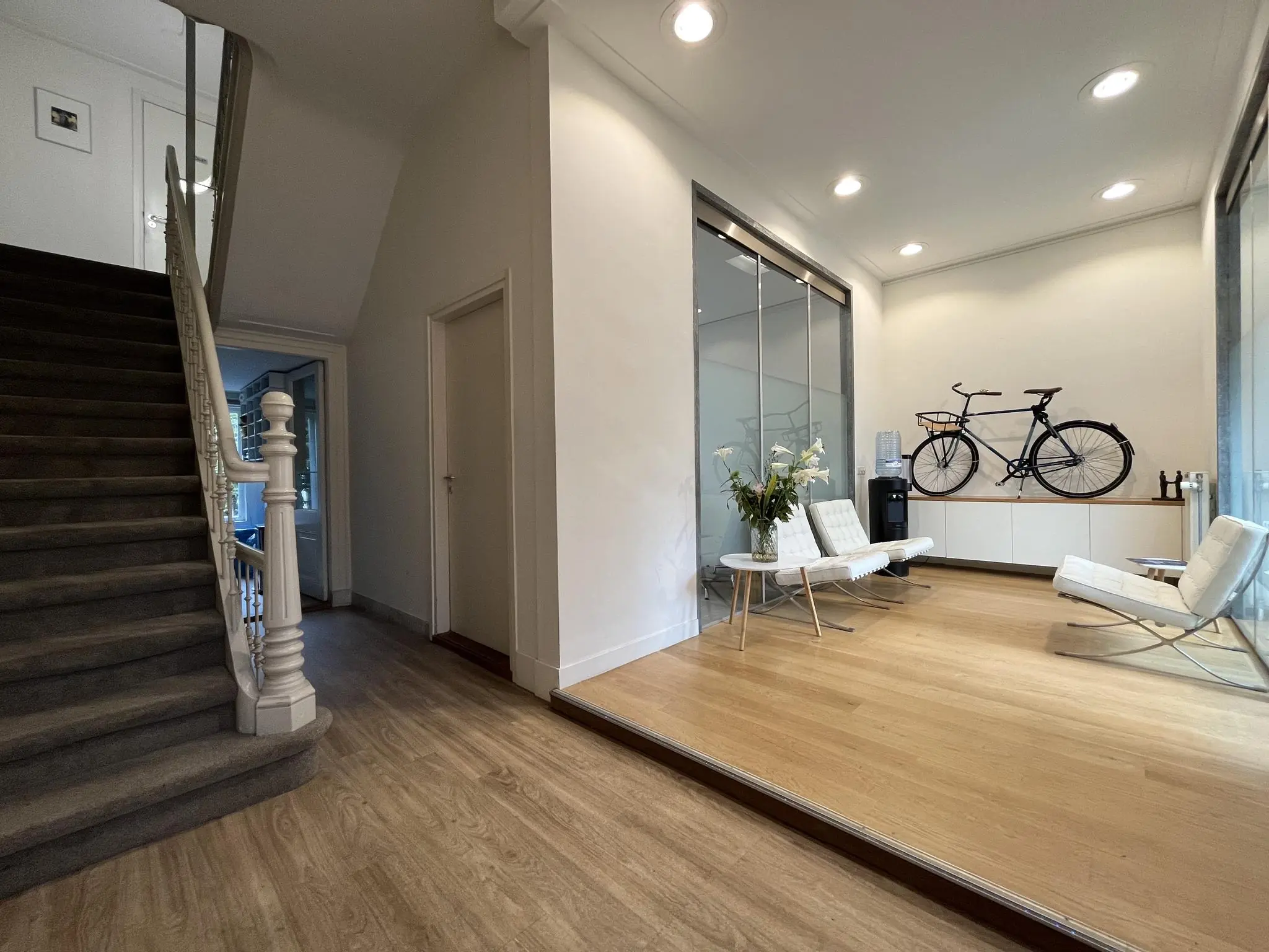 Moderne wachtruimte aan de Ramstraat met witte stoelen, een zwarte fiets aan de muur en een trap naar boven.