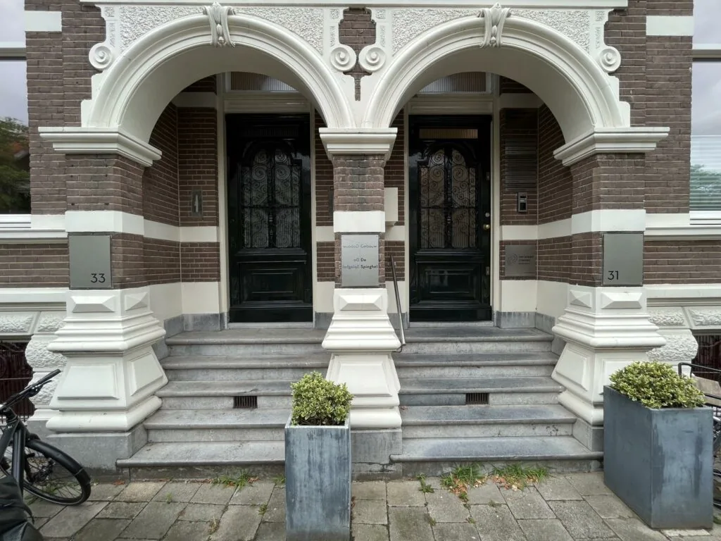 Twee identieke historische entrees met bogen en trappen van panden aan de Ramstraat, genummerd 31 en 33.