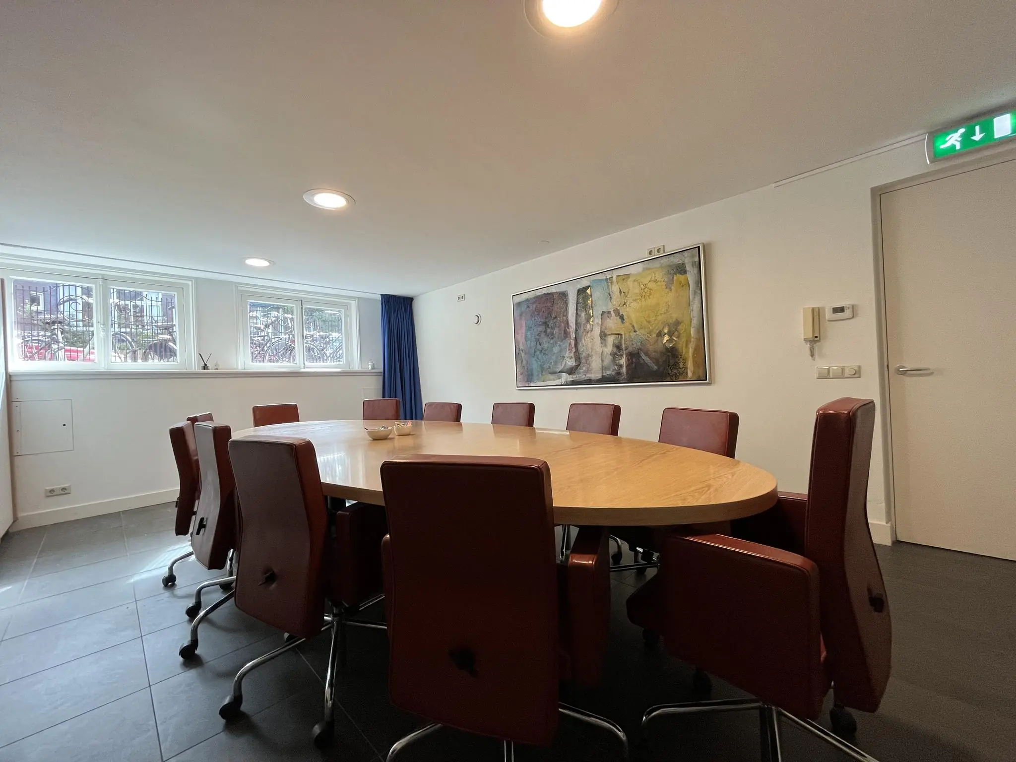 Vergaderruimte aan de Ramstraat met ovale houten tafel, rode stoelen en abstract schilderij aan de muur.