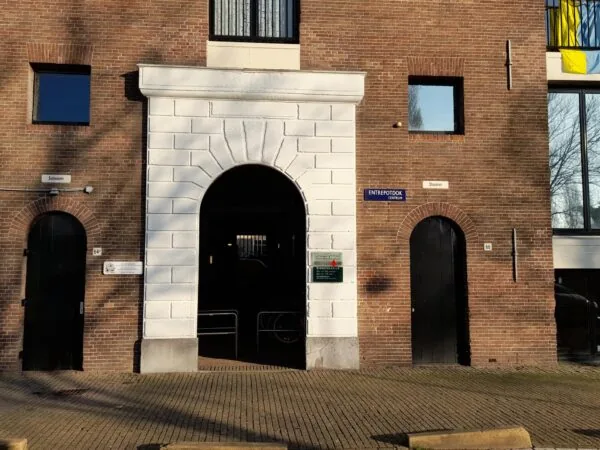 Ingang van een historisch bakstenen gebouw aan het Entrepotdok in Amsterdam met een witte boog en zwarte deuren.