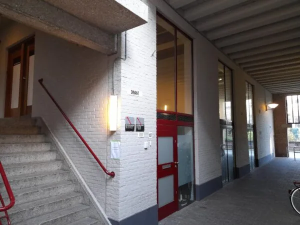 Ingang van het woongebouw aan het Entrepotdok met witte bakstenen, rode deur en trap met rood leuningwerk.