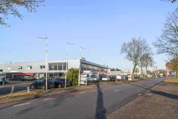 Bedrijventerrein aan de Nijverheidsweg met parkeerplaatsen, bedrijfsgebouwen en langsrijdende auto's op een zonnige dag.