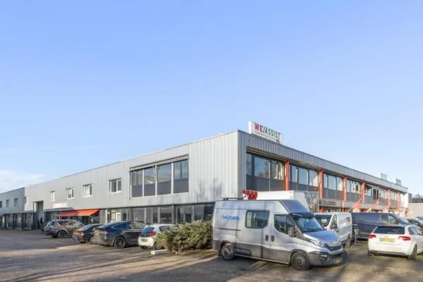 Bedrijfsverzamelgebouw aan de Nijverheidsweg met geparkeerde auto's en bestelbussen op de voorgrond.