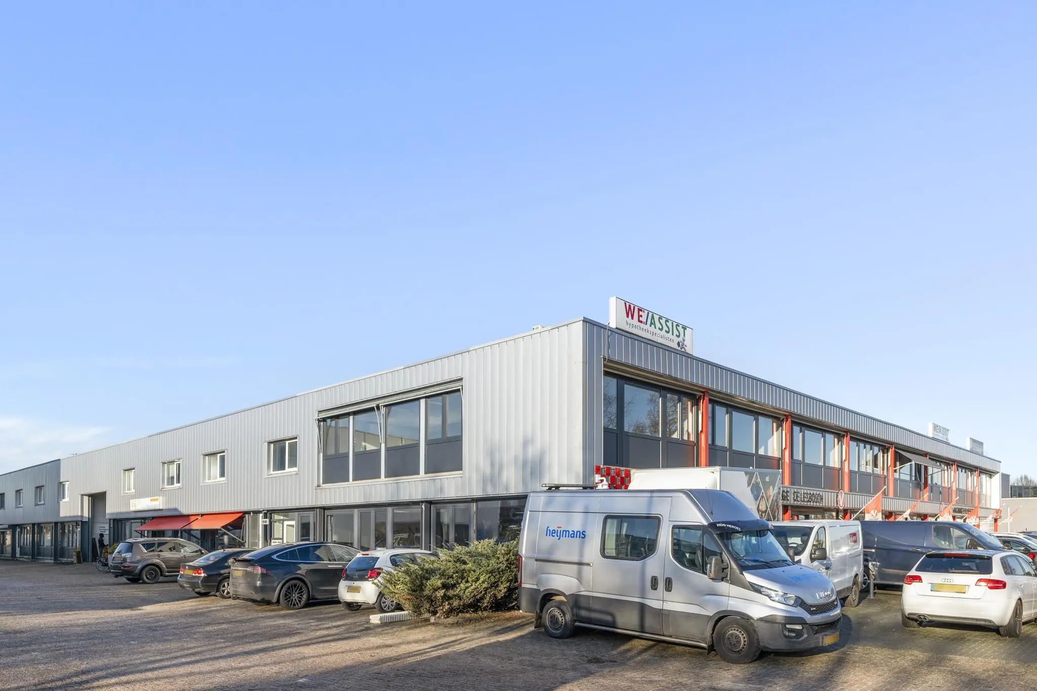 Bedrijfsverzamelgebouw aan de Nijverheidsweg met geparkeerde auto's en bestelbussen op de voorgrond.