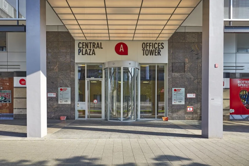 Ingang van het Central Plaza Offices Tower-gebouw aan het Weena in Rotterdam met een draaideur en naamborden.