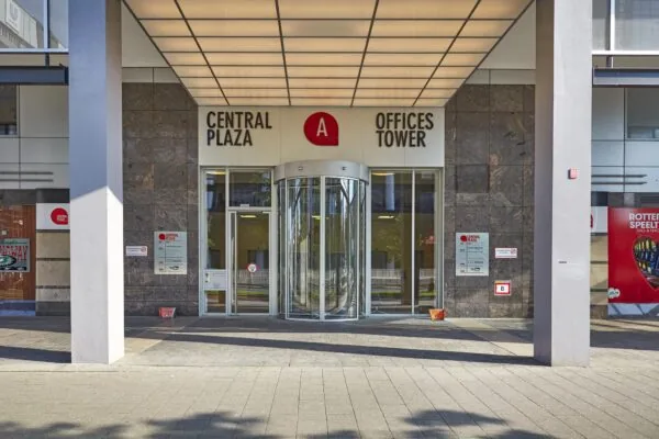 Ingang van het Central Plaza Offices Tower-gebouw aan het Weena in Rotterdam met een draaideur en naamborden.