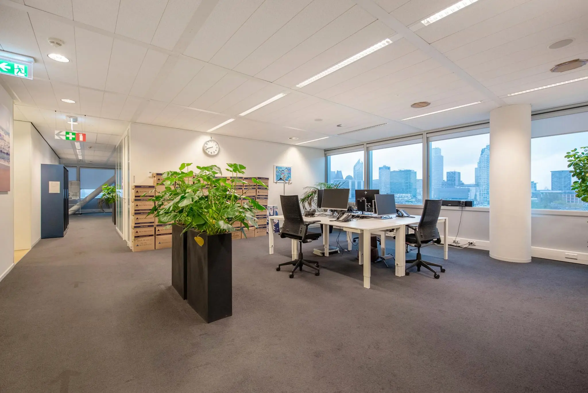 Modern kantoorinterieur aan de Schenkkade met bureaus, planten en uitzicht op de skyline van Den Haag.