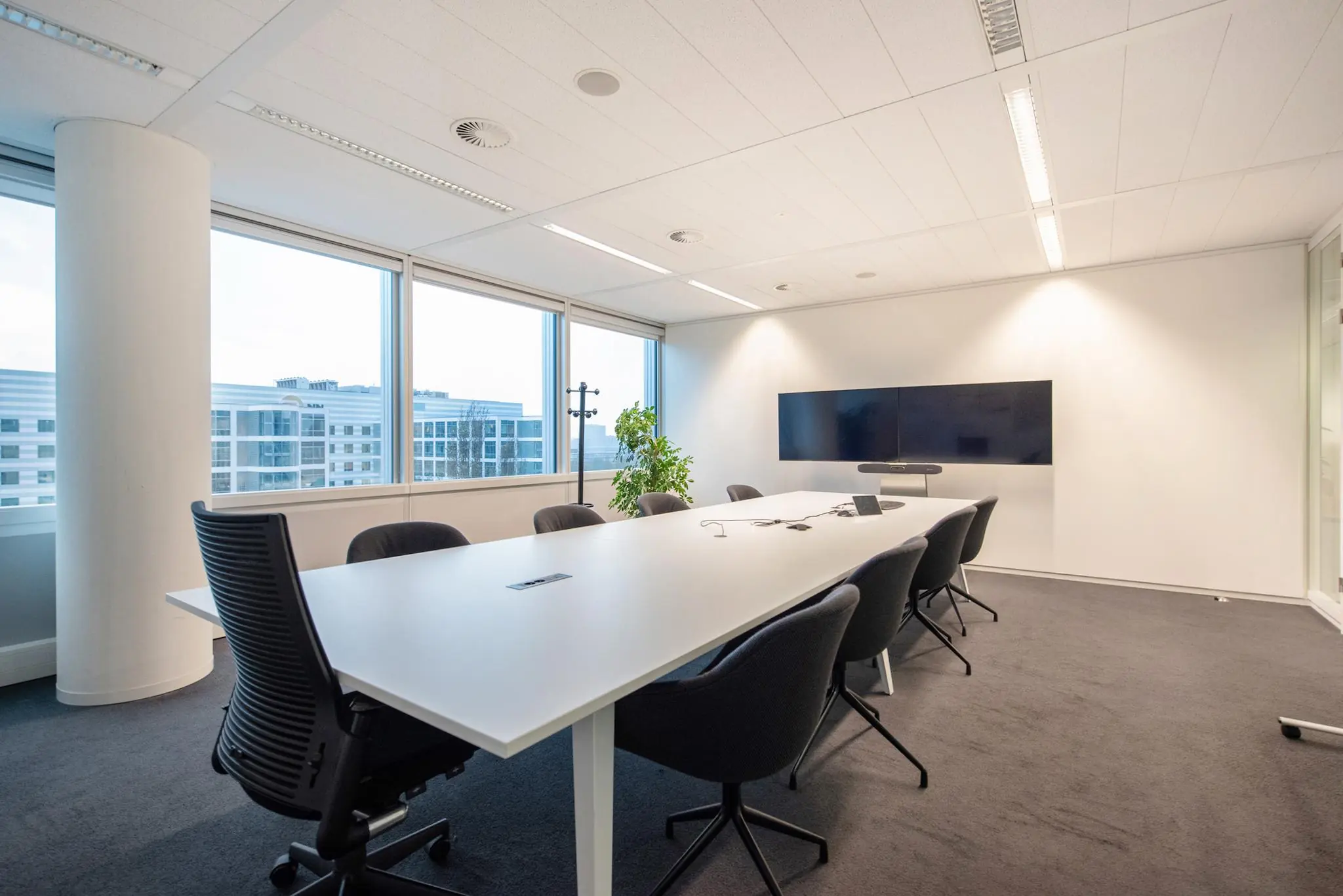 Moderne vergaderruimte aan de Schenkkade met lange tafel, zwart meubilair en groot videoscherm aan de muur.