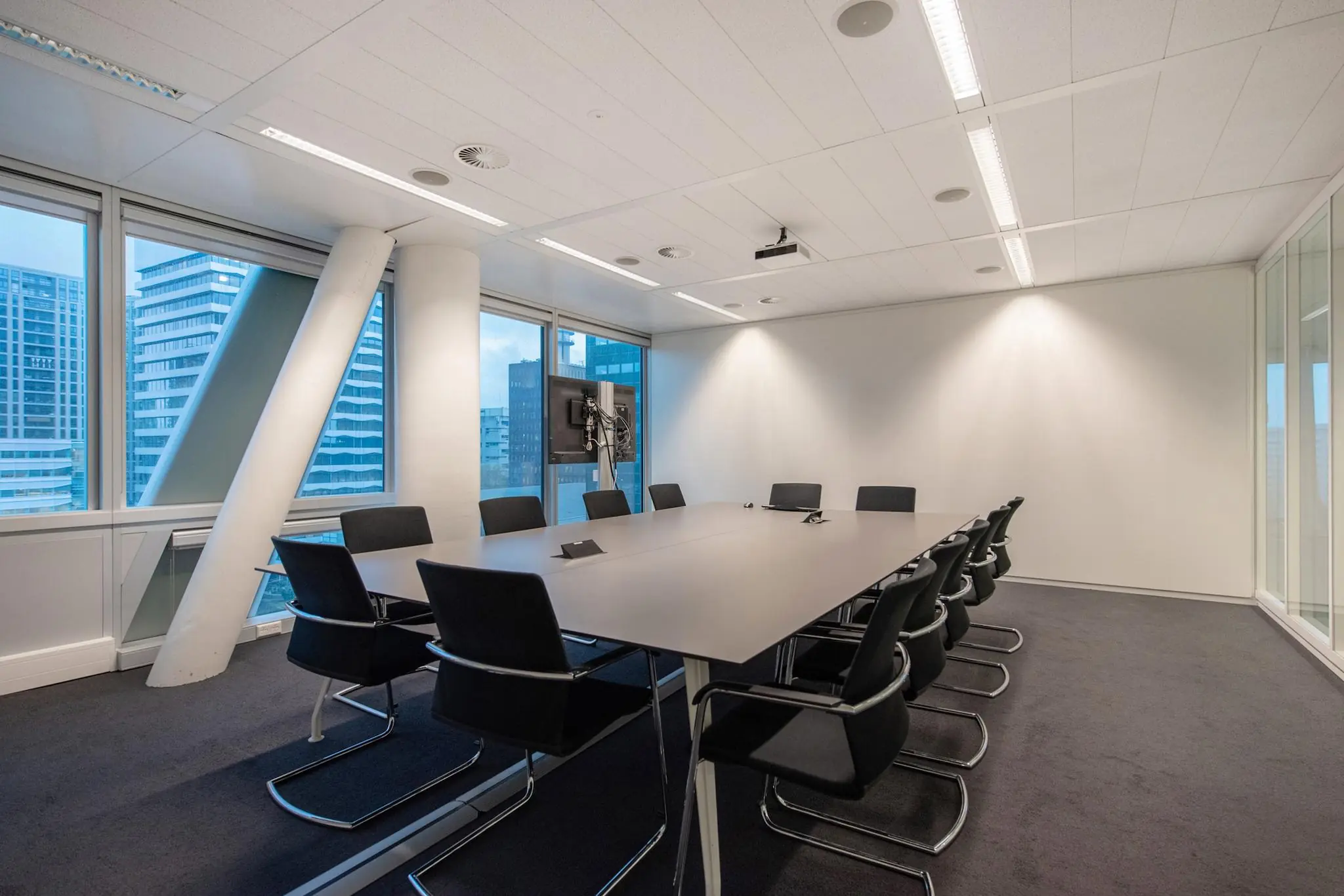 Moderne vergaderzaal met een grote tafel, twaalf stoelen en uitzicht op hoge gebouwen aan de Schenkkade.