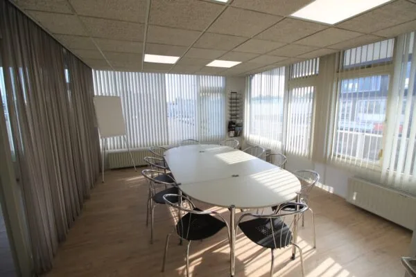 Vergaderruimte met ovale tafel, metalen stoelen, flip-over en grote ramen met verticale lamellen aan de Nevadadreef.