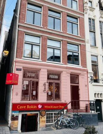 Voorgevel van een pand aan het Rokin met een wijn- en gedistilleerdwinkel genaamd "Cave Rokin" op de begane grond en een tatoeage- en piercingstudio op de eerste verdieping.