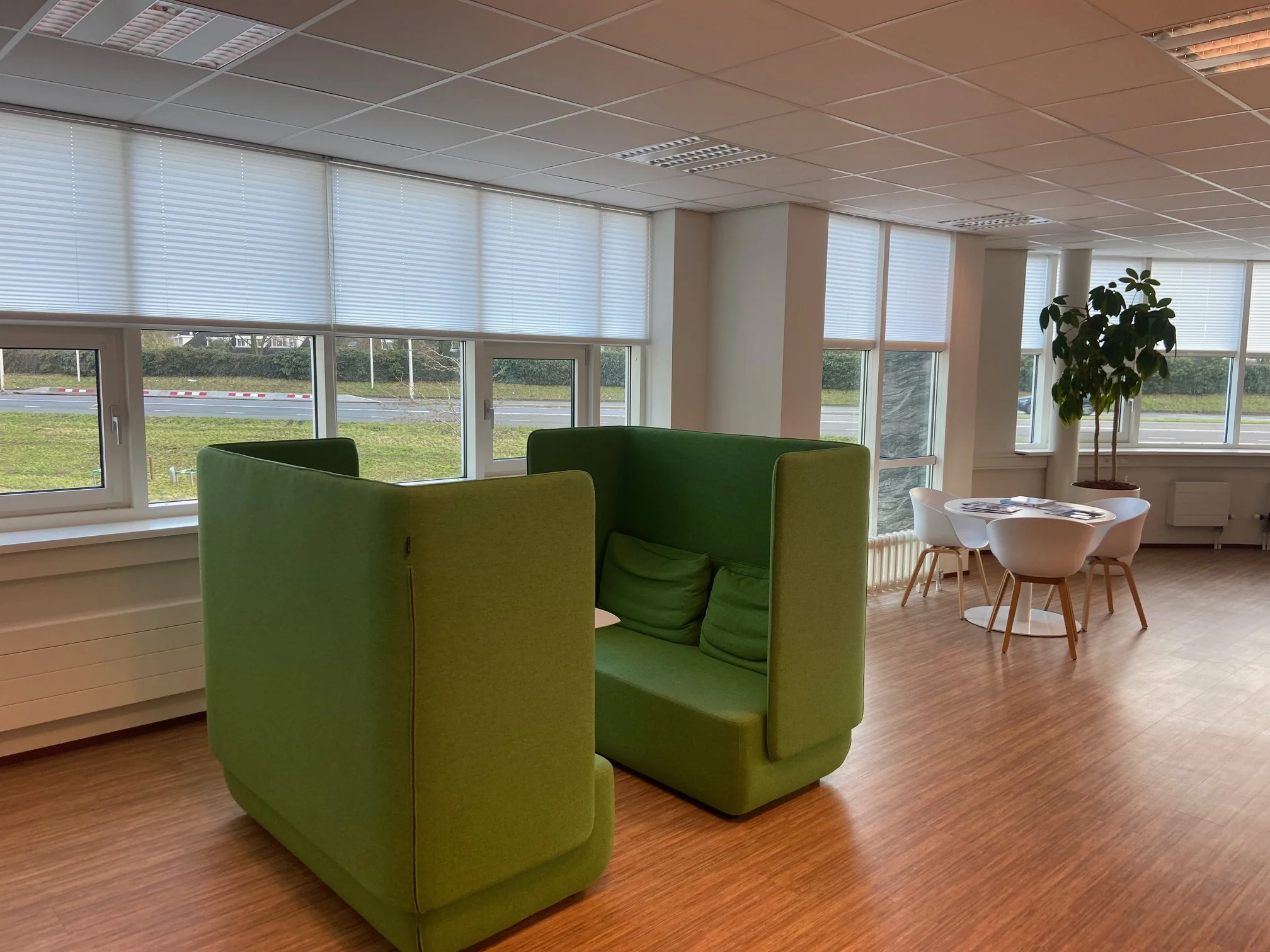 Moderne kantoorruimte aan het Rhijnspoor met groene zitbank, ronde tafel en grote ramen met jaloezieën.