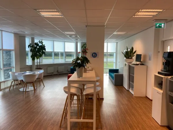 Moderne en lichte kantoorkantine aan de Rhijnspoorweg met zitplekken, planten en een koffieautomaat.