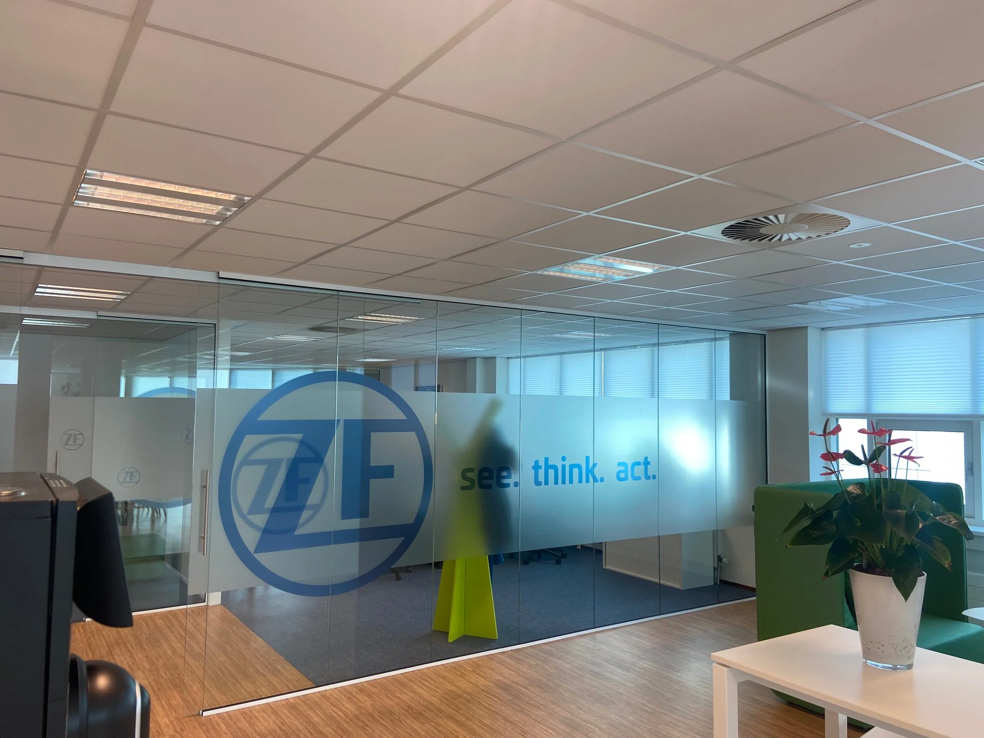Moderne kantoorruimte in het Rhijnspoorgebouw met glazen wanden waarop het ZF-logo en de slogan "see. think. act." te zien zijn.