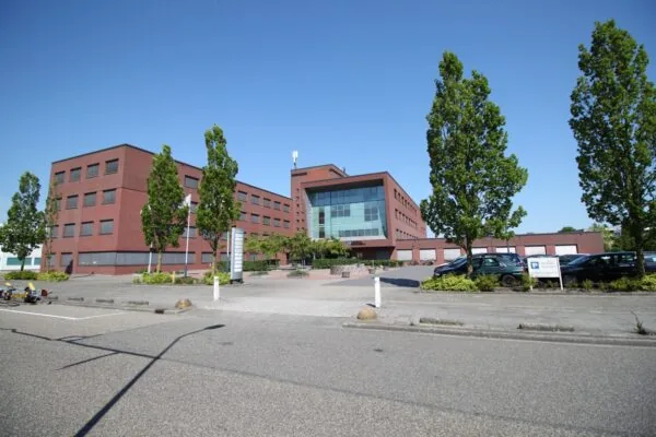 Zakelijk kantoorgebouw aan de Pompmolenlaan met bakstenen gevel en grote ramen, omgeven door bomen en parkeerplaatsen.