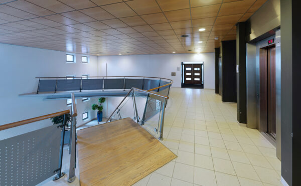 Moderne en lichte hal op de eerste verdieping van een kantoorgebouw aan de Pompmolenlaan, met een trap, lift en glazen balustrade.