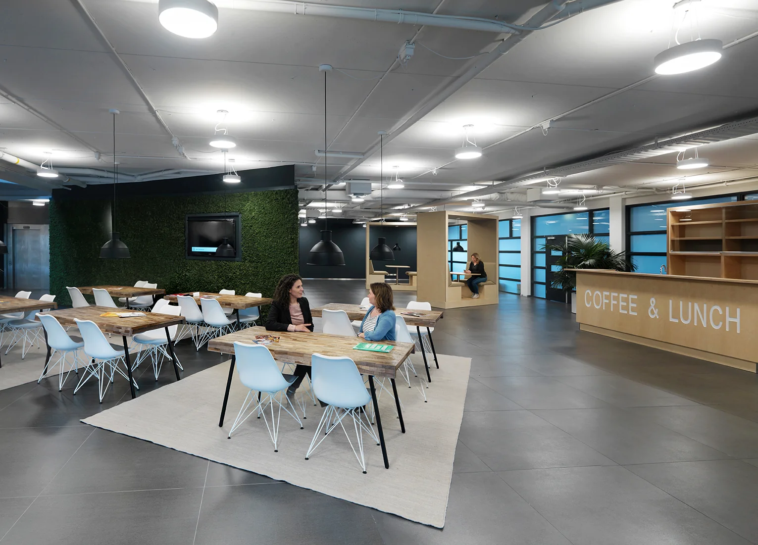 Moderne bedrijfslounge aan de Pompmolenlaan met houten tafels, witte stoelen en een koffie- en lunchbalie.