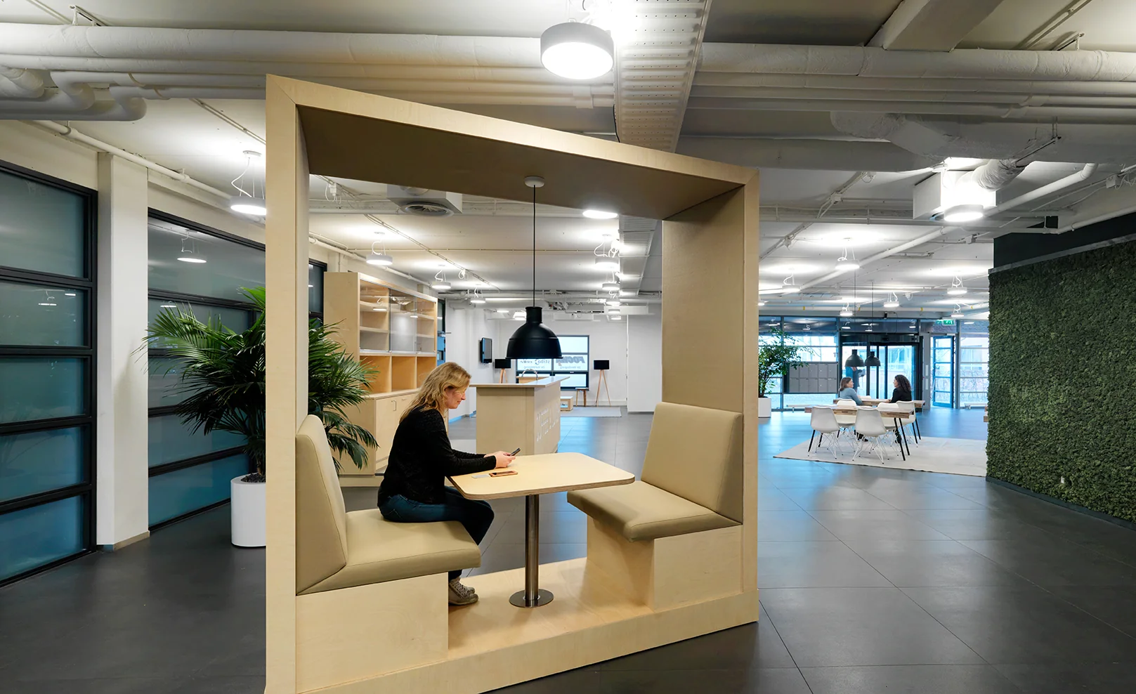 Vrouw werkt op een laptop in een moderne kantoorruimte aan de Pompmolenlaan, zittend in een houten nis met ingebouwde zitbanken.